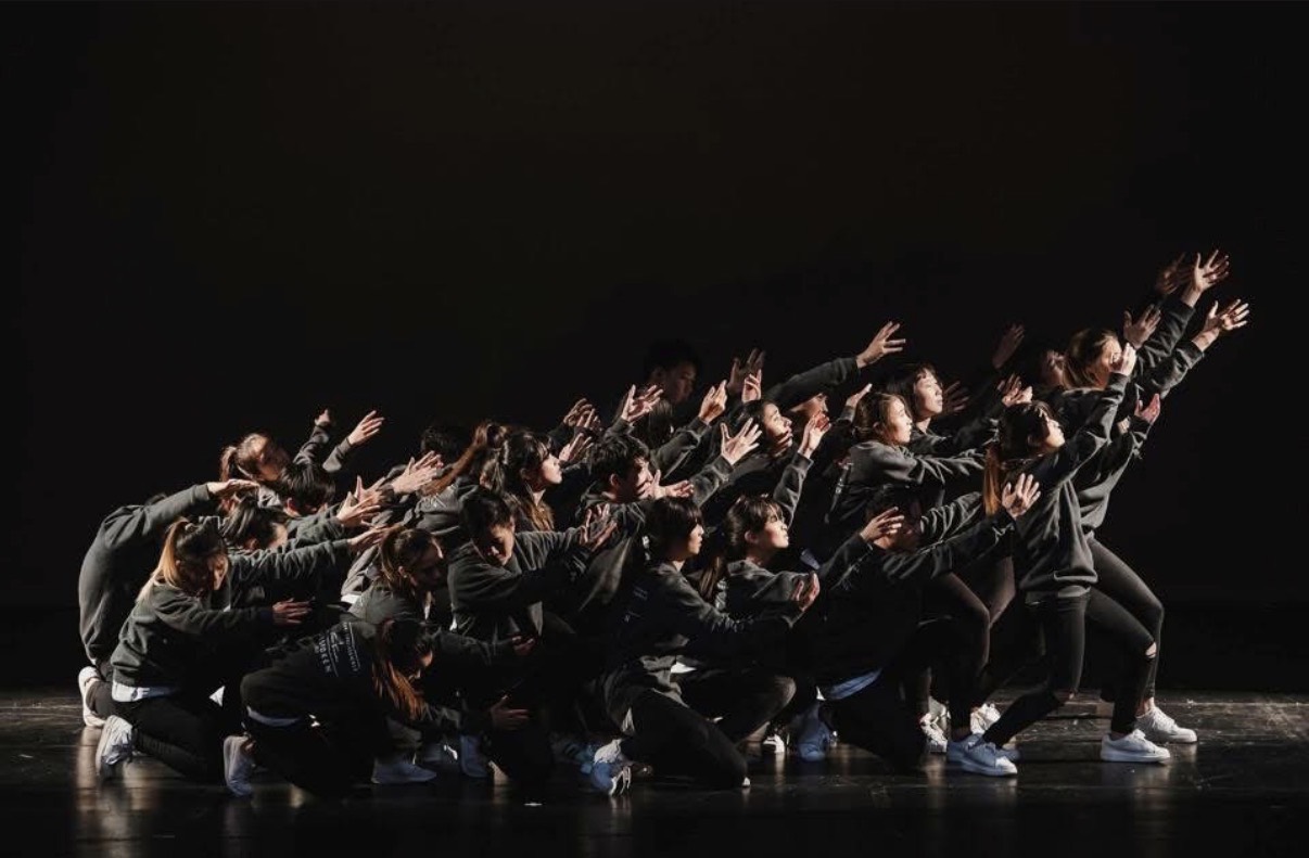 The Feels ensemble reaching together across a dark stage