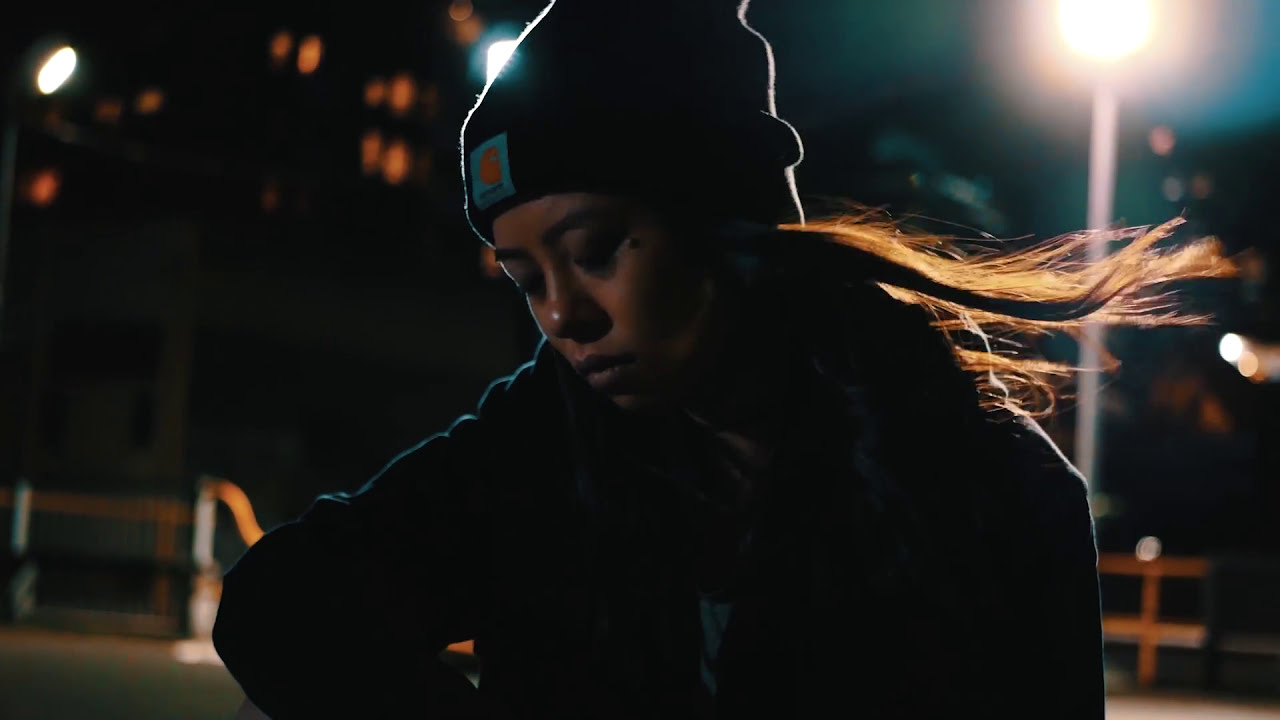 A dancer in a beanie lit against the night in Old English